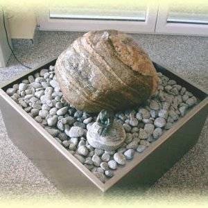 Besonders       schön gemaserter beiger Granit-Quellstein auf hellgrauem Zierkies  in       Edelstahl-Becken (Größe 80/80/35 cm)